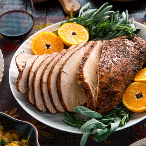 Smoked turkey breast served on a large platter along with tangerine halves and herbs.