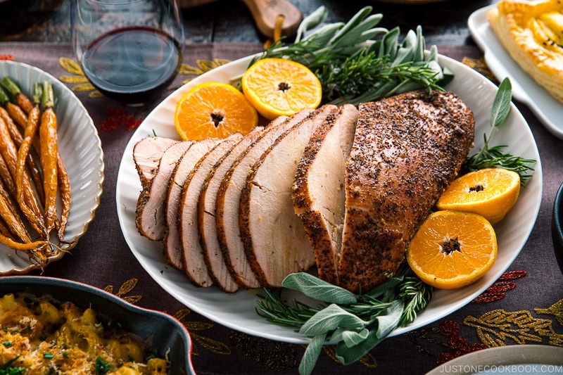 Smoked turkey breast served on a large platter along with tangerine halves and herbs.