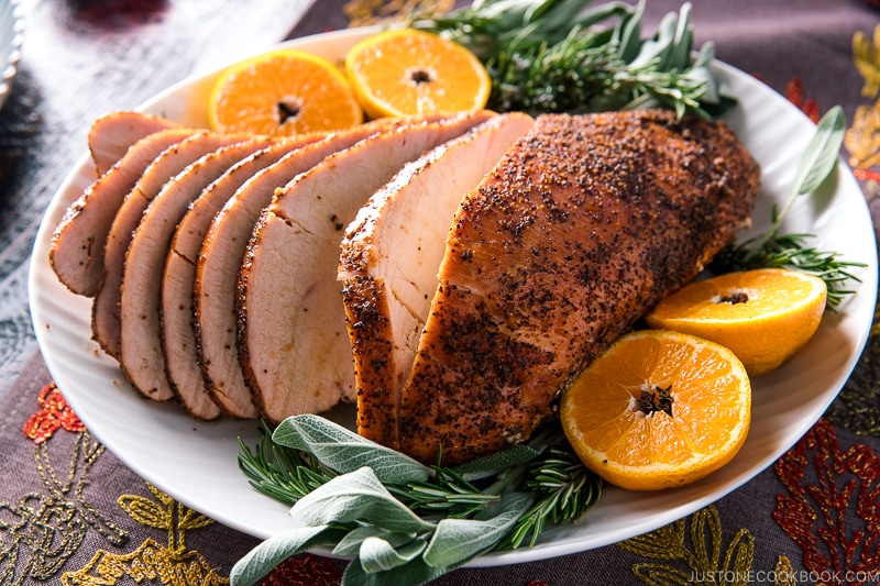 Smoked turkey breast served on a large platter along with tangerine halves and herbs.