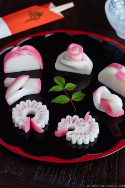 Decorative kamaboko fish cakes on a black and red lacquered board.