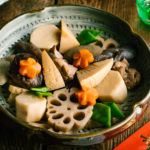 A Japanese ceramic bowl containing simmered chicken and vegetables.