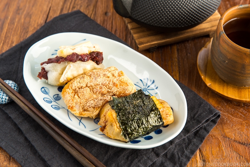 A rectangular plate containing three flavors of mochi (sweet red bean, sweet soybean flour, and soy sauce and nori seaweed).