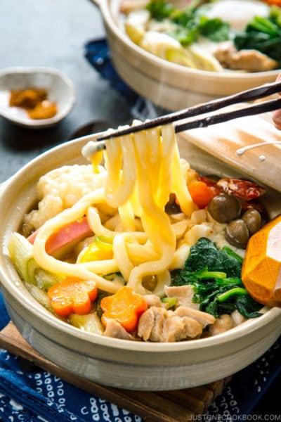 Donabe containing udon noodles, chicken, fish cake, mushrooms, and vegetables in a flavorful soup broth