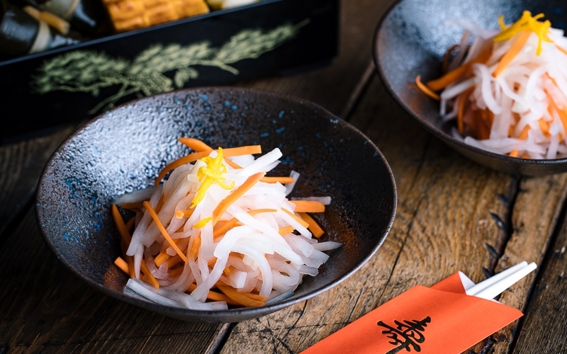 A black bowl containing Namasu (Japanese Daikon and Carrot Salad).