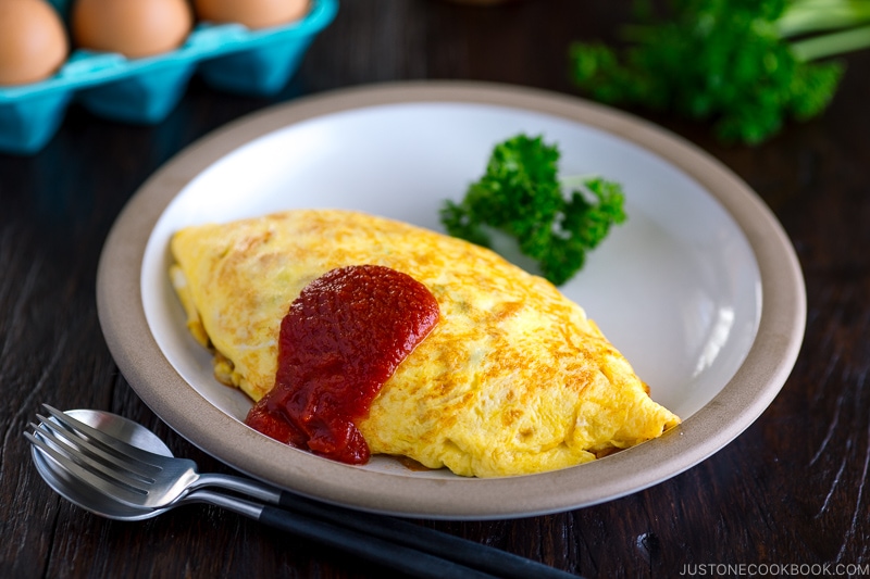 A plate containing omurice and tomato sauce on top.