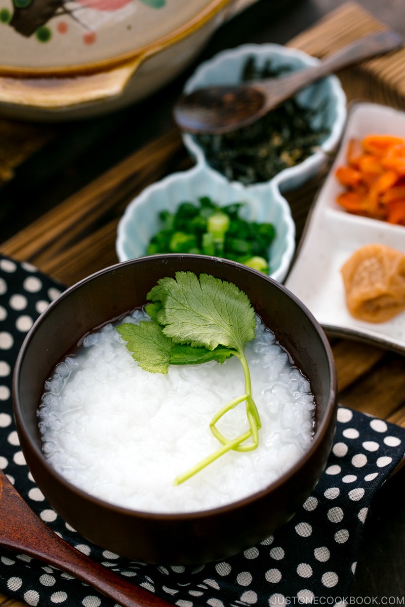 Bouillie de riz japonaise servie dans un bol avec du saumon, des oignons verts, des prunes marinées et des algues déchiquetées.