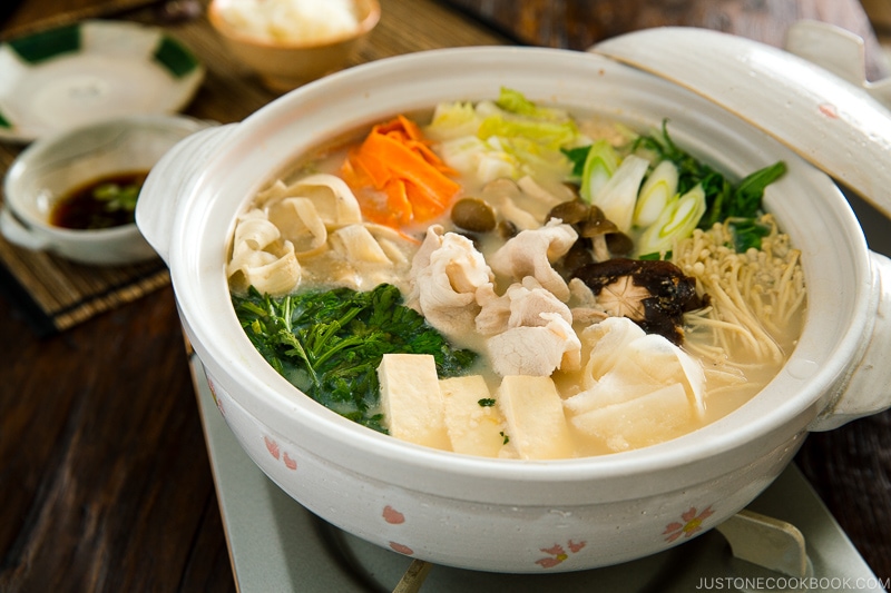 A donabe containing vegetables and pork in a savory miso soy milk broth.