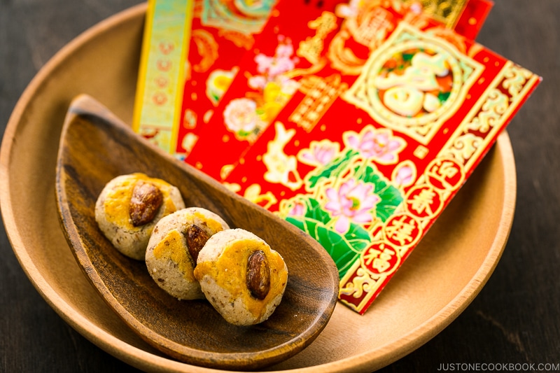 Chinese almond cookies and red envelops on a wooden tray.