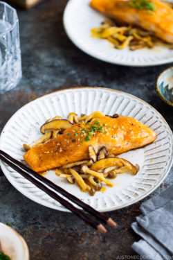 A white plate containing Miso Butter Salmon served with sautéed shiitake and shimeji mushrooms.