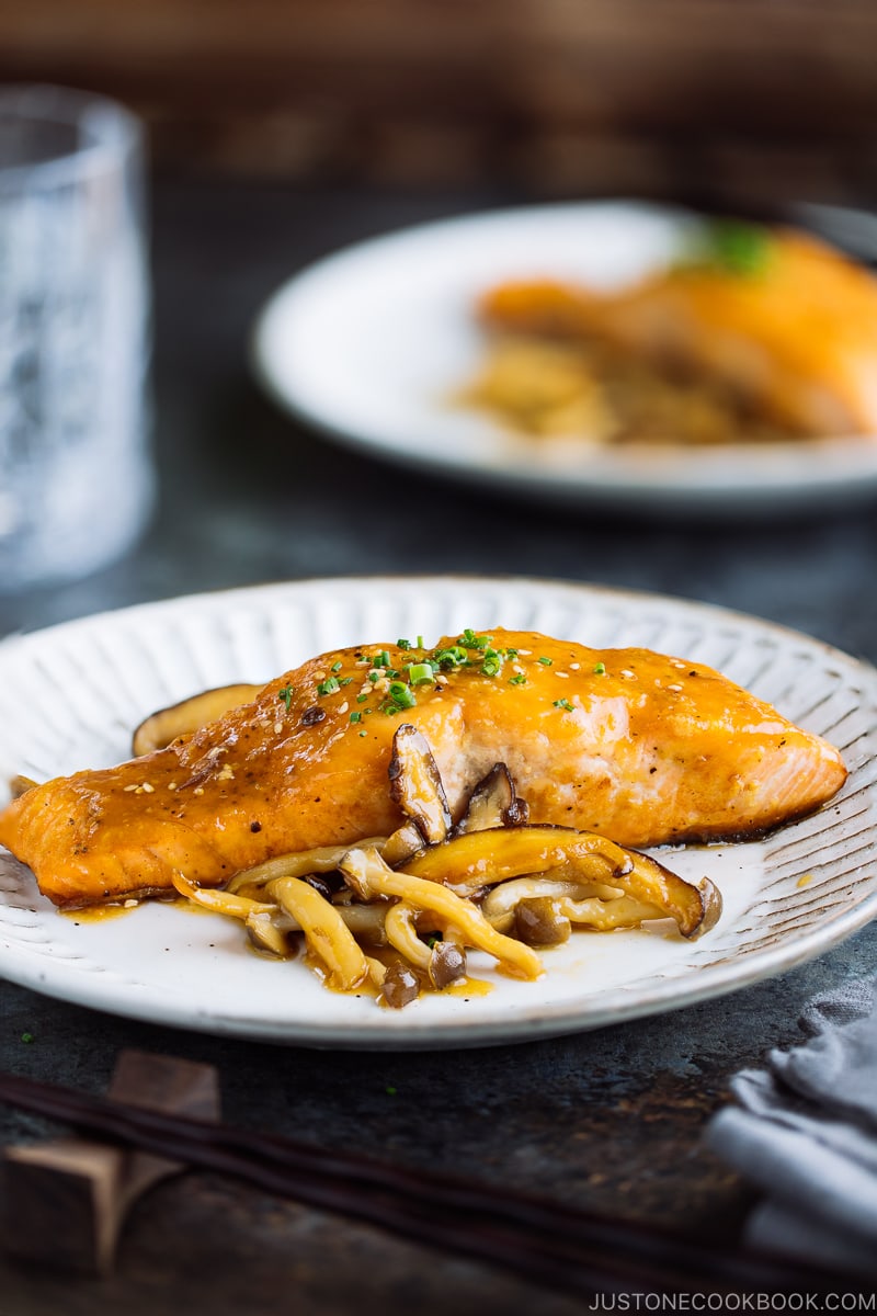 A white plate containing Miso Butter Salmon served with sautéed shiitake and shimeji mushrooms.