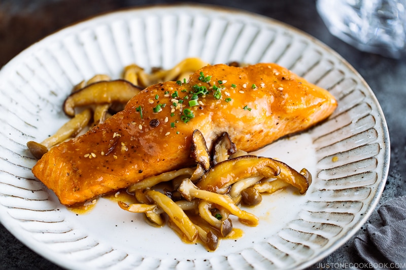 A white plate containing Miso Butter Salmon served with sautéed shiitake and shimeji mushrooms.