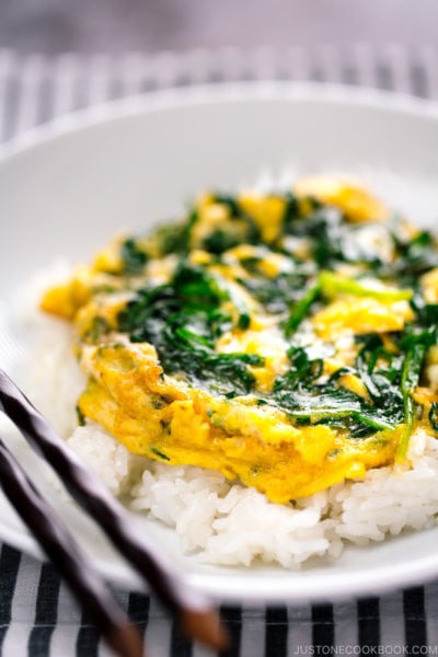 A white bowl containing a soft fluffy egg stir fry with Chinese chive served over steamed rice.