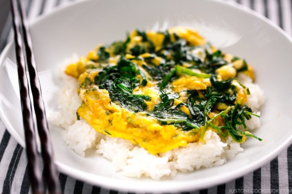 A white bowl containing a soft fluffy egg stir fry with Chinese chive served over steamed rice.