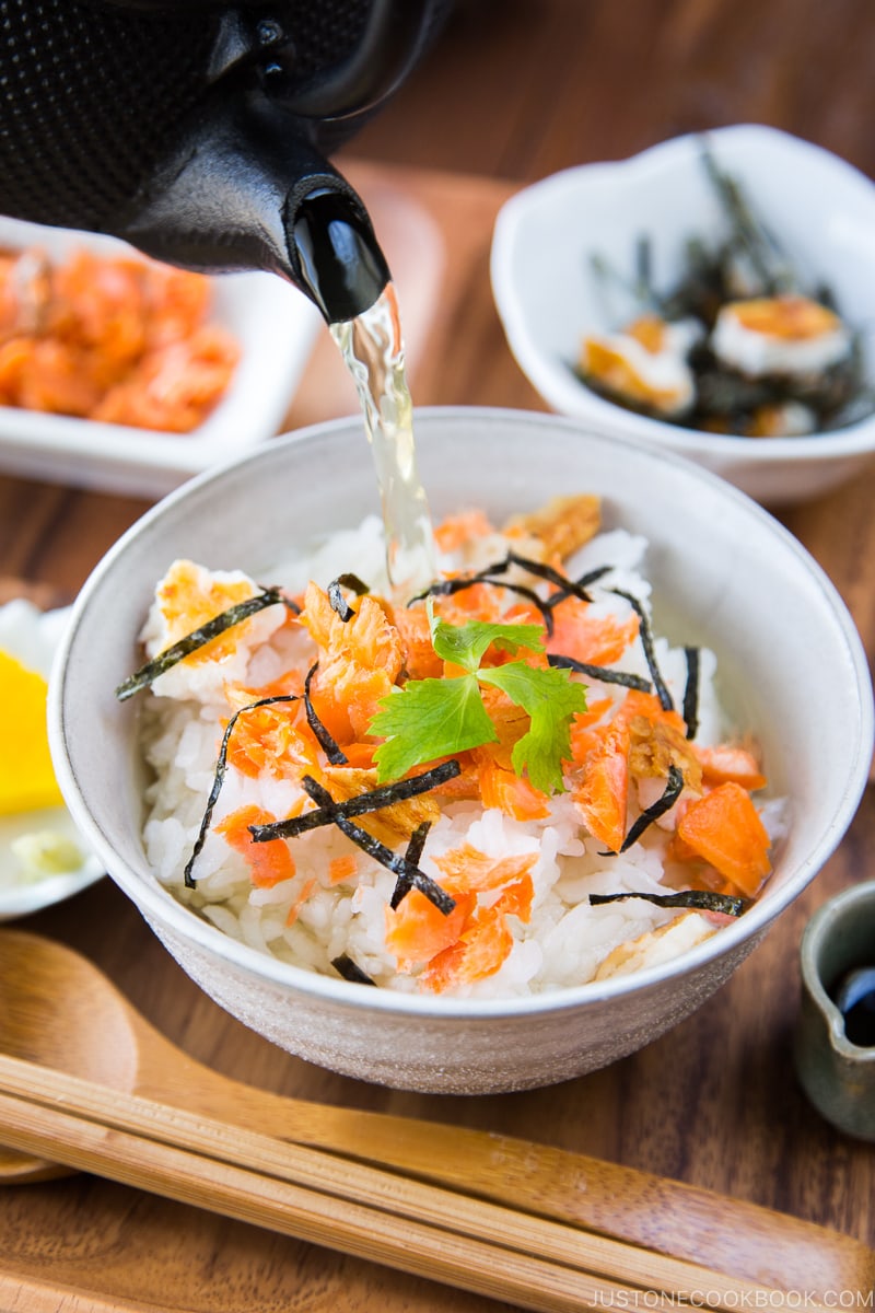 Le thé japonais est versé sur du riz cuit à la vapeur et du saumon cuit feuilleté dans un bol de riz.