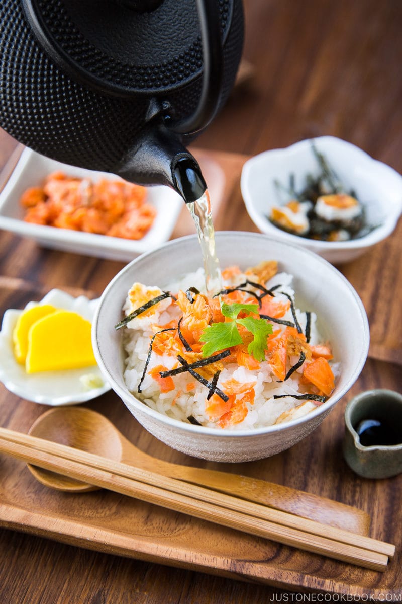 Japanese tea is poured on top of steamed rice and flaky baked salmon in a rice bowl.