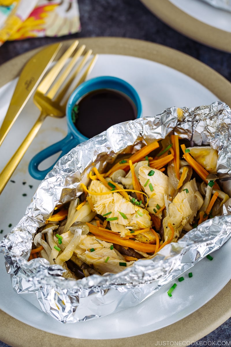 Une assiette contenant du saumon en papillote avec une sauce ponzu sur le côté.