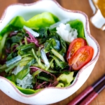White ceramic bowls containing seaweed salad and miso dressing.