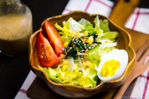 A wooden bowl containing green salad with Japanese sesame dressing.