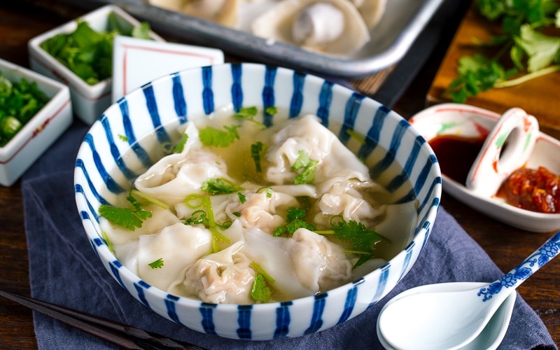 a large bowl containing shrimp and wonton soup along with the condiments.