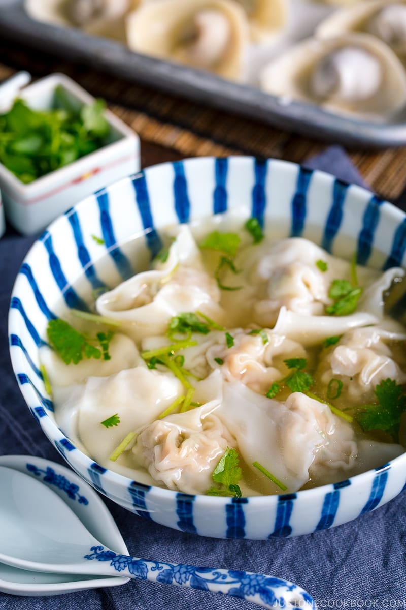 a large bowl containing shrimp and wonton soup along with the condiments.