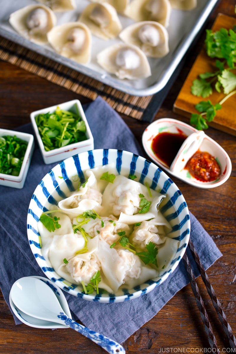 a large bowl containing shrimp and wonton soup along with the condiments.