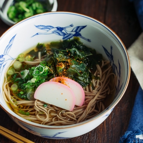 A Japanese bowl containing Toshikoshi Soba Noodle Soup with fish cake and wakame seaweed.