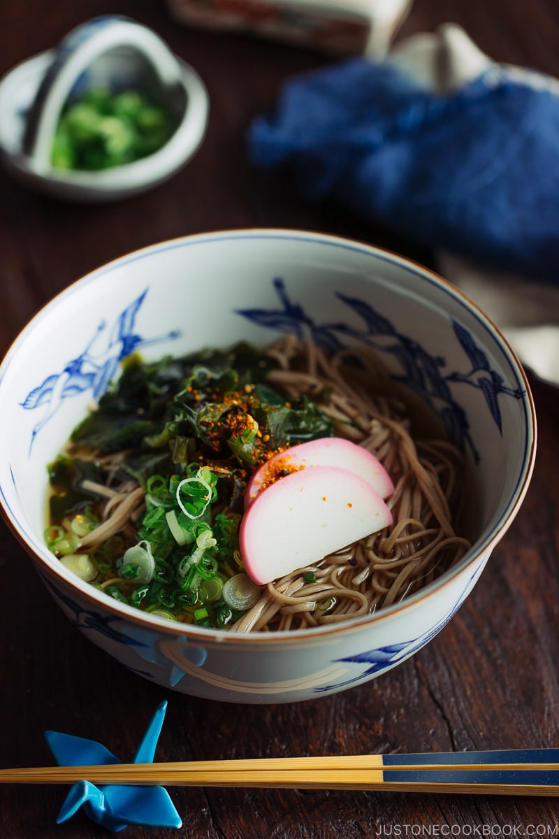 A Japanese bowl containing Toshikoshi Soba Noodle Soup with fish cake and wakame seaweed.