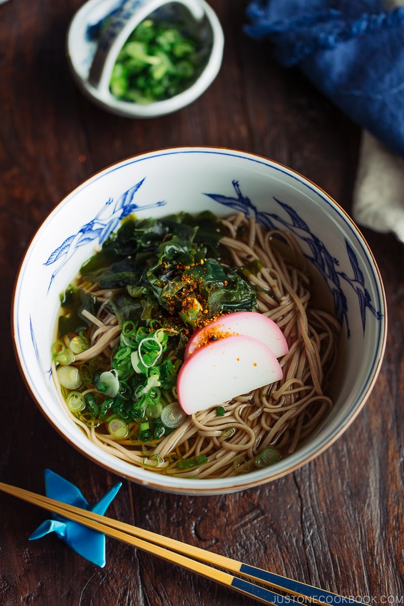 A Japanese bowl containing Toshikoshi Soba Noodle Soup with fish cake and wakame seaweed.