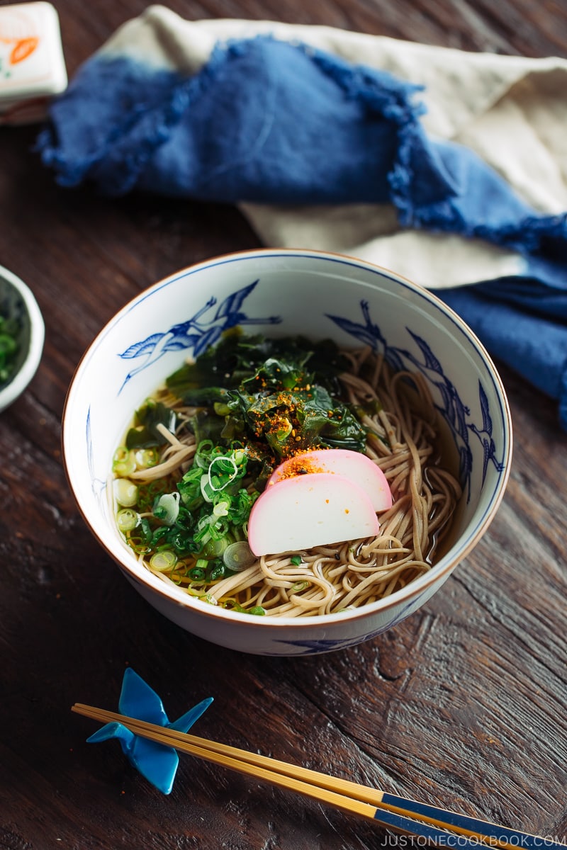 A Japanese bowl containing Toshikoshi Soba Noodle Soup with fish cake and wakame seaweed.