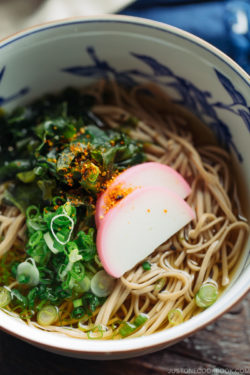 A Japanese bowl containing Toshikoshi Soba Noodle Soup with fish cake and wakame seaweed.