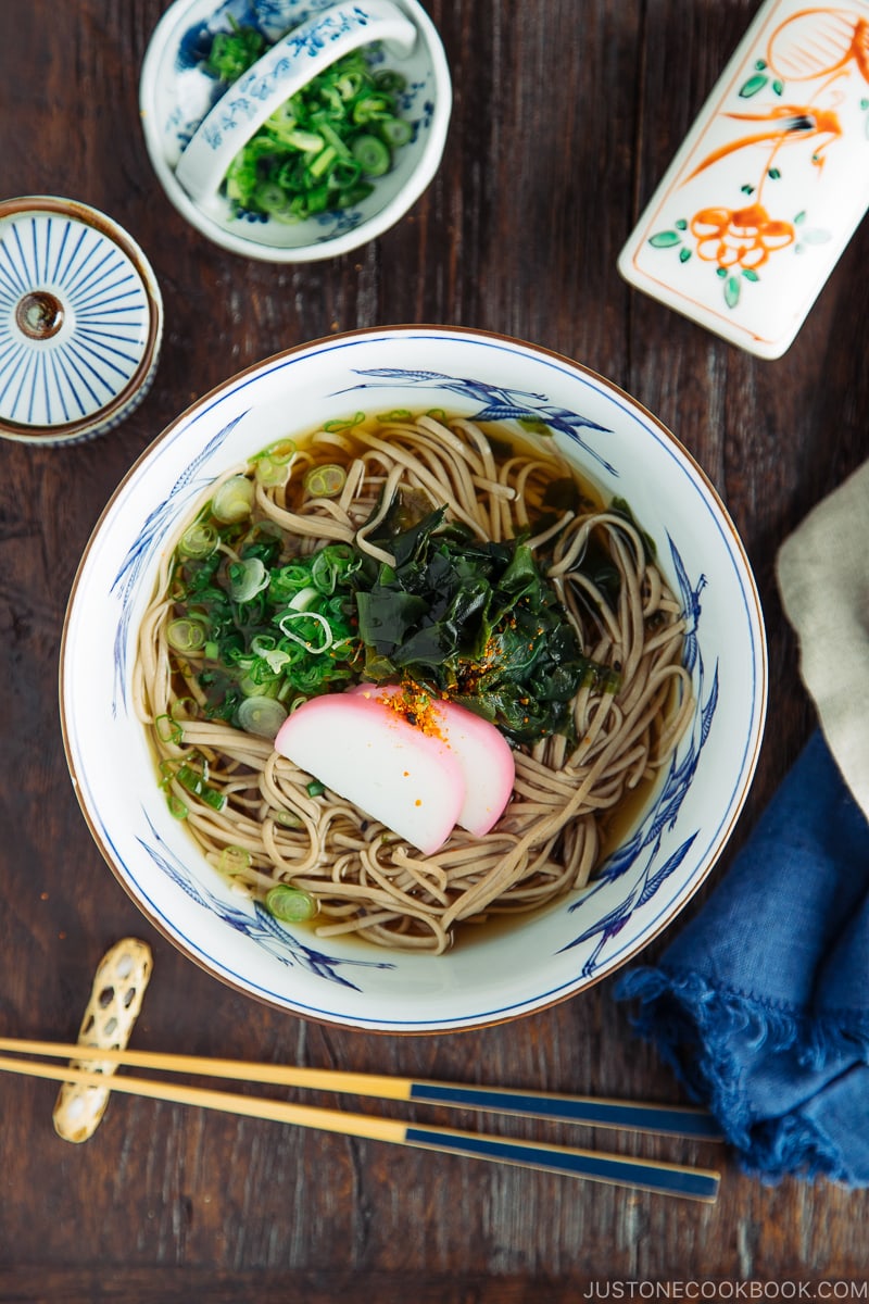 A Japanese bowl containing Toshikoshi Soba Noodle Soup with fish cake and wakame seaweed.