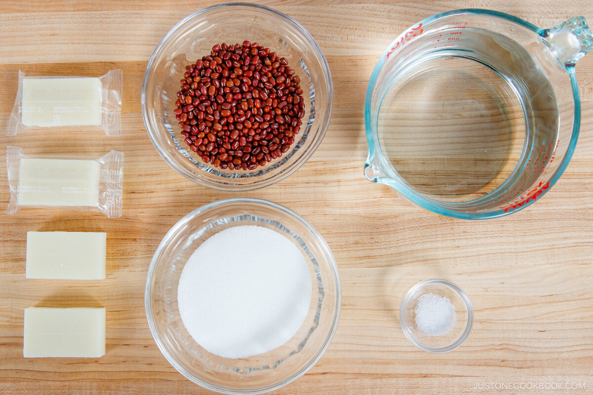 three blocks of butter, two bowls with red beans and sugar, a glass measuring cup with water, and a small bowl of salt.