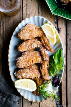 A platter of fried chicken wings garnished with lemon and green salad.