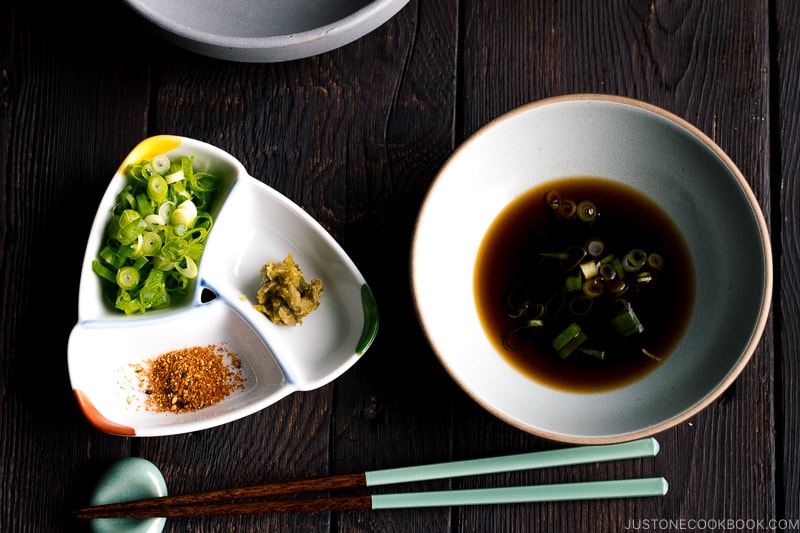 Dipping sauce and condiments to go with, including green onion, yuzu kosho, shichimi togarashi.