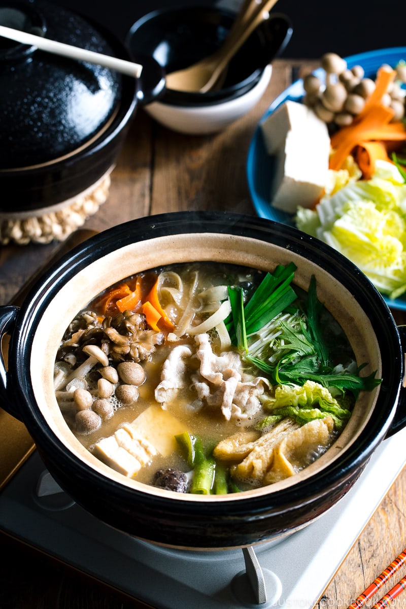 A Japanese earthenware pot (Donabe) containing vegetables, tofu, and pork cooked in sesame and miso based soup broth.