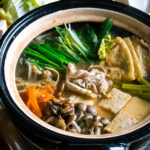 A Japanese earthenware pot (Donabe) containing vegetables, tofu, and pork cooked in sesame and miso based soup broth.