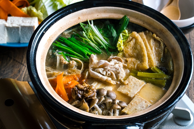 A Japanese earthenware pot (Donabe) containing vegetables, tofu, and pork cooked in sesame and miso based soup broth.