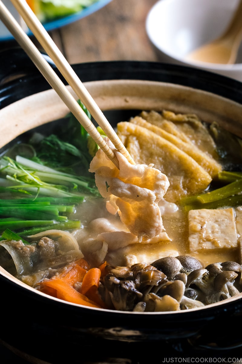 A Japanese earthenware pot (Donabe) containing vegetables, tofu, and pork cooked in sesame and miso based soup broth.