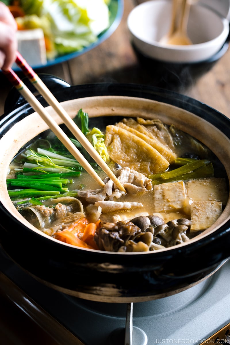 A Japanese earthenware pot (Donabe) containing vegetables, tofu, and pork cooked in sesame and miso based soup broth.