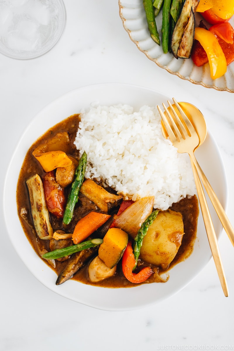 Un piatto bianco contenente curry giapponese vegetariano insieme a riso al vapore.