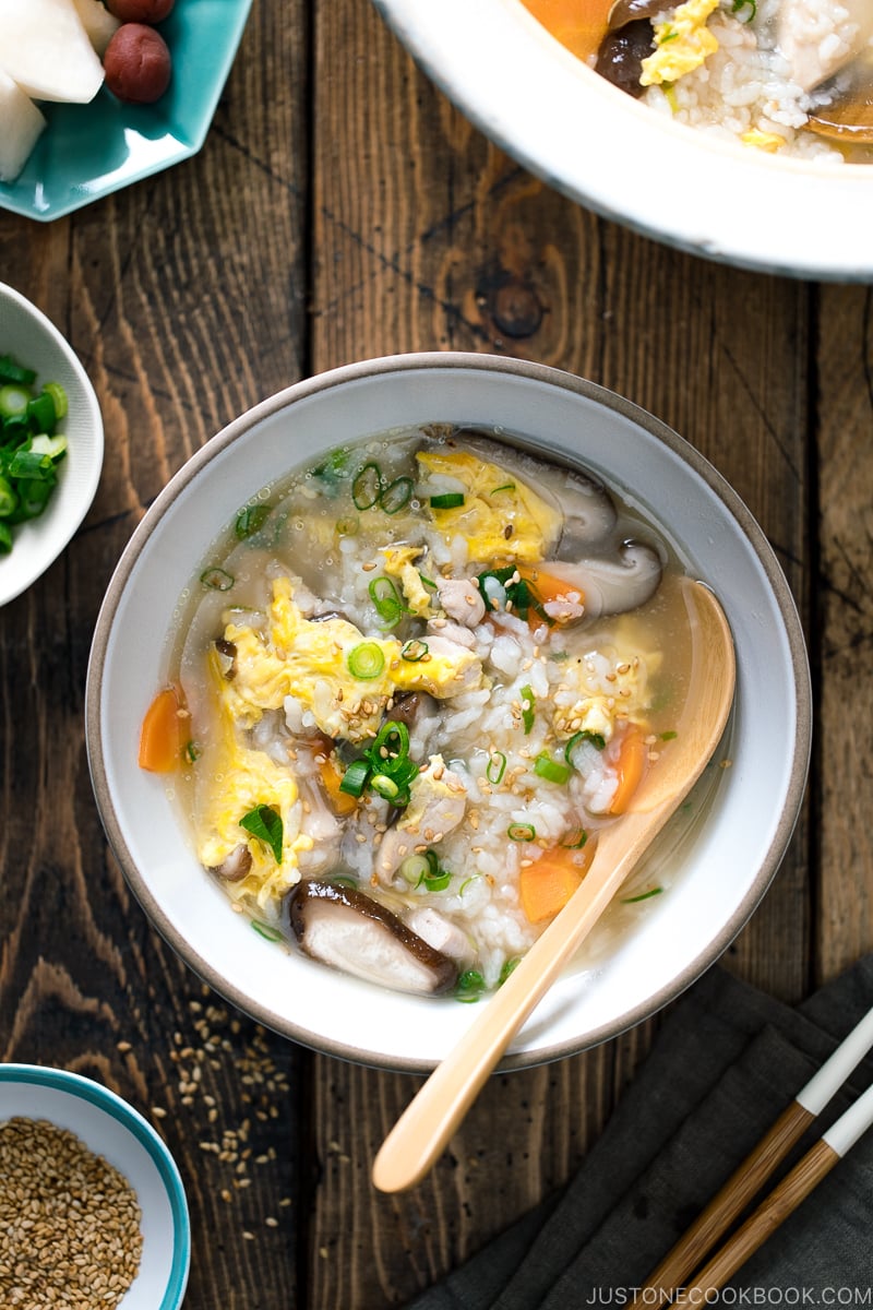 Chicken Zosui (Japanese rice soup) served in a white ceramic bowl along with green onions and sesame seeds in a separate bowl.