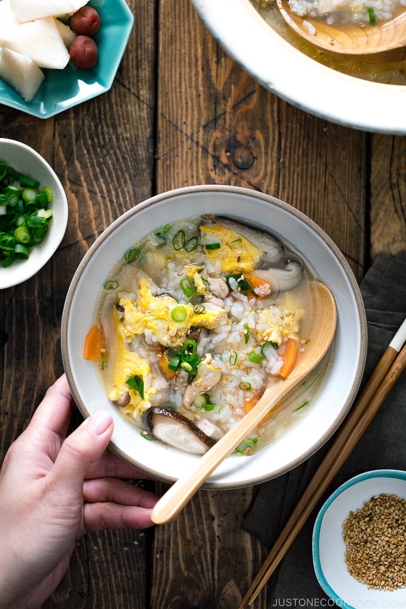 Poulet Zosui (soupe de riz japonaise) servi dans un bol en céramique blanche avec des oignons verts et des graines de sésame dans un bol séparé.