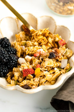 A white bowl containing homemade granola with blackberries.
