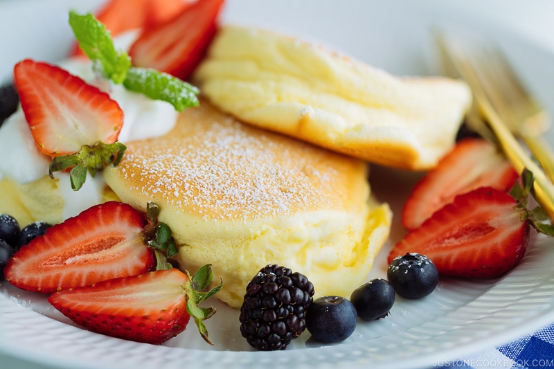 A white plate containing fluffy Japanese souffle pancakes, fresh berries, and whipped cream.
