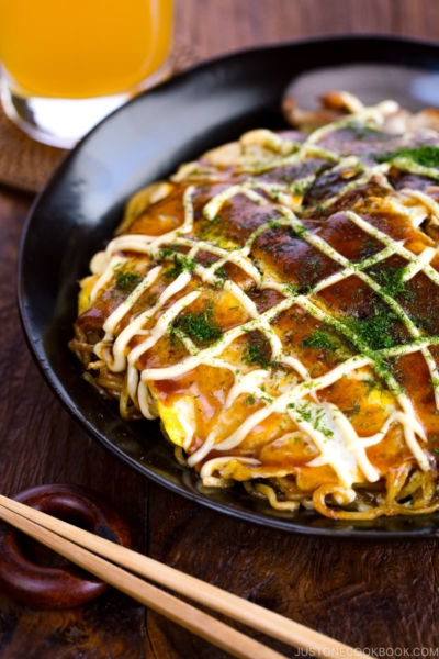 A black plate containing Hiroshima-style OKonomiyaki topped with the savory sauce and Japanese mayo.