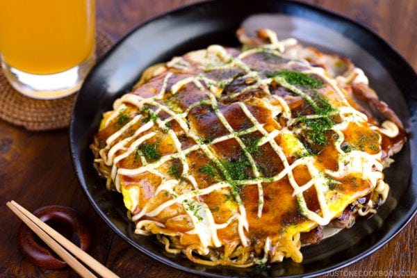 A black plate containing Hiroshima-style OKonomiyaki topped with the savory sauce and Japanese mayo.