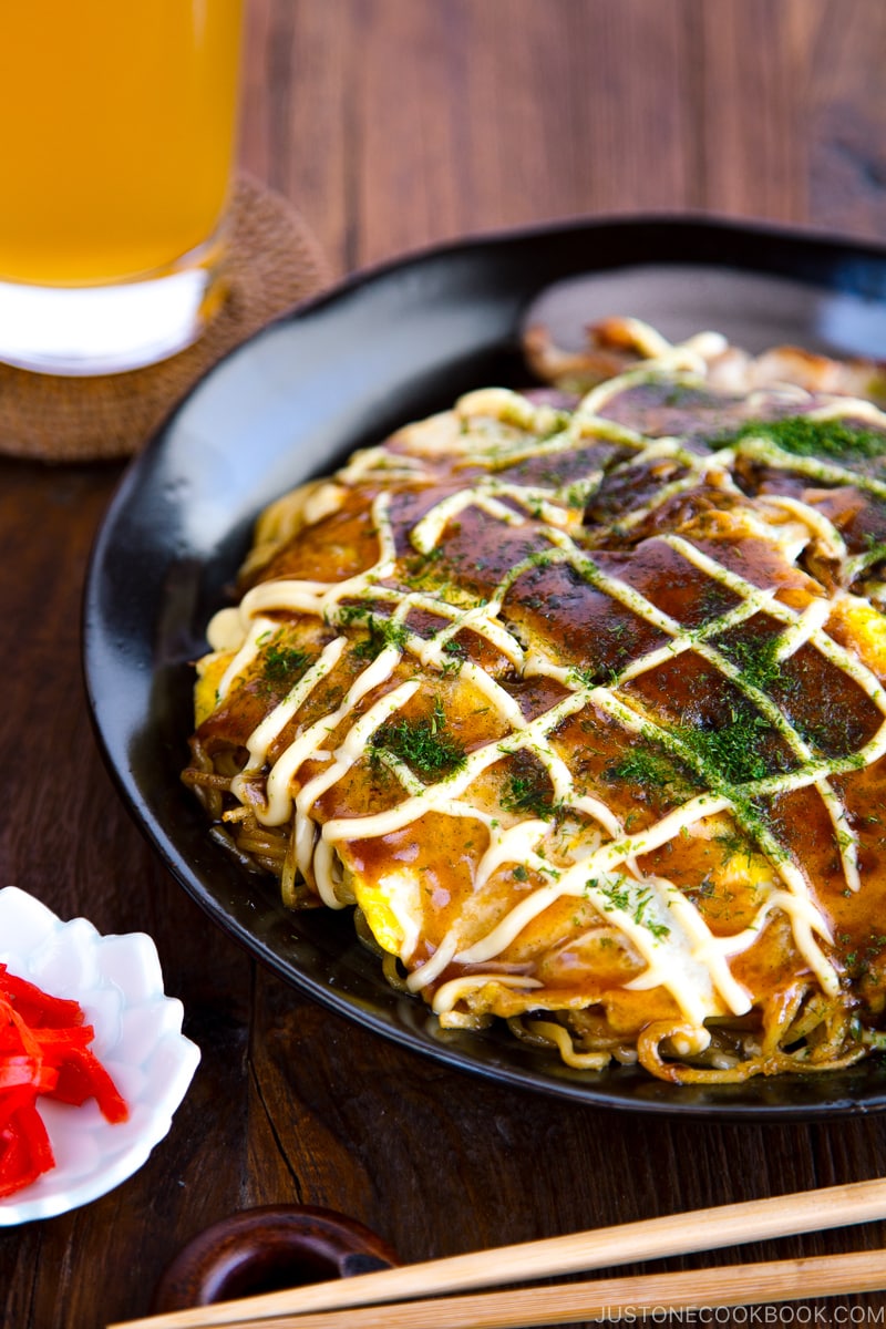 A black plate containing Hiroshima-style OKonomiyaki topped with the savory sauce and Japanese mayo.