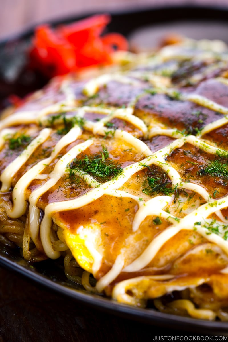 A black plate containing Hiroshima-style OKonomiyaki topped with the savory sauce and Japanese mayo.