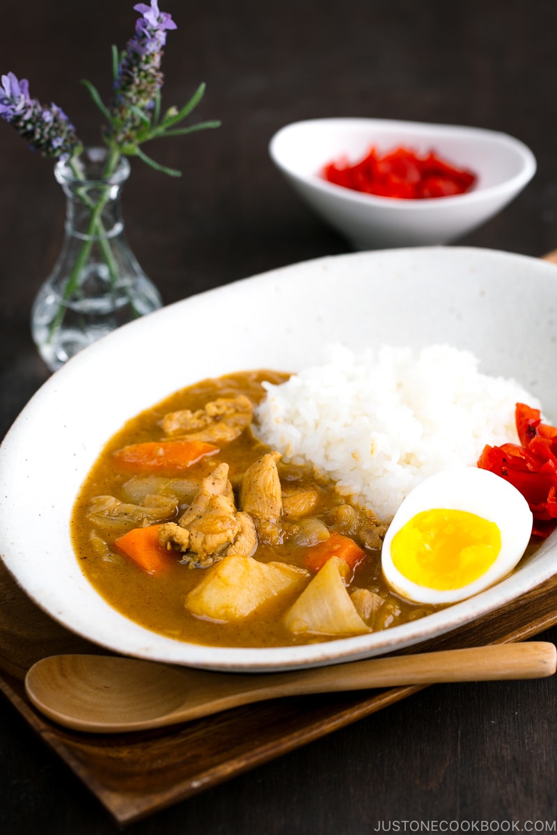 A white oval-shaped plate containing Japanese Chicken Curry topped with egg and pickles.