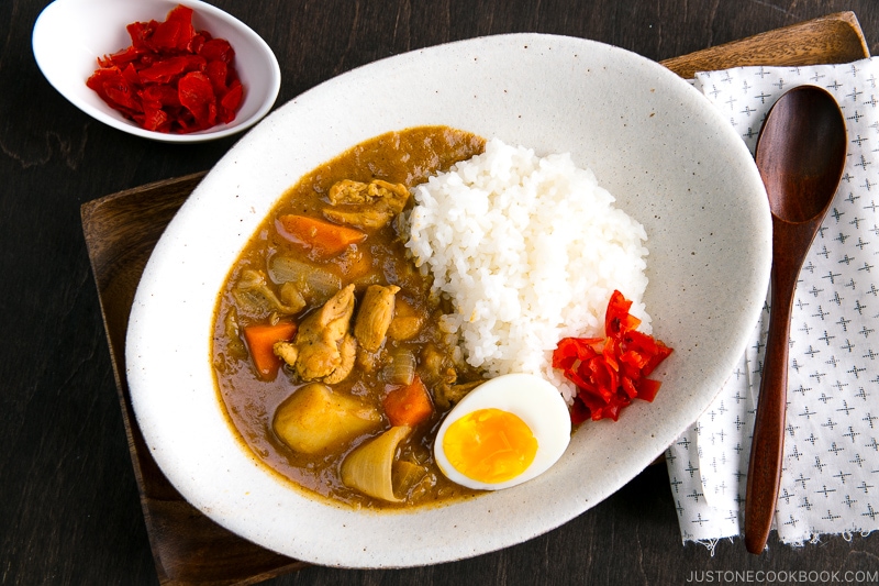 A white oval-shaped plate containing Japanese Chicken Curry topped with egg and pickles.